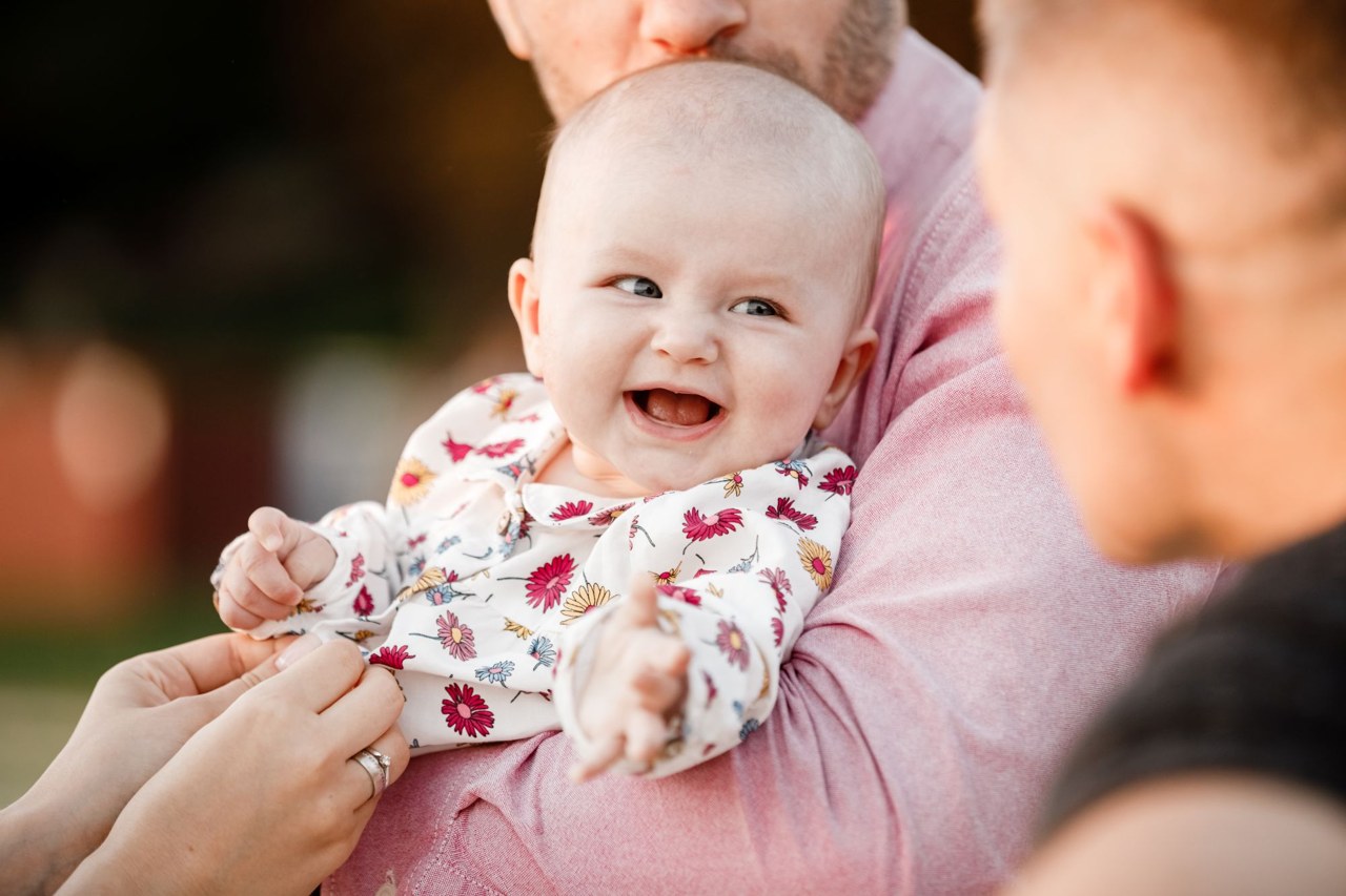 A smiling baby cradled by parents outdoors — a happy, well-rested moment between Australian wake windows